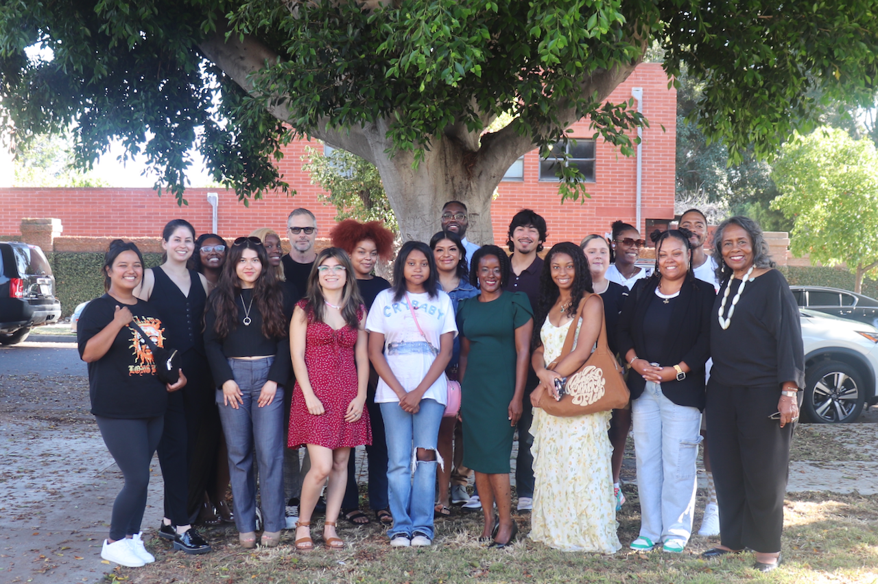 A multiethnic, multi-aged group of people who have received the Biddy Mason Charitable Foundation scholarship are assembled under a tree.