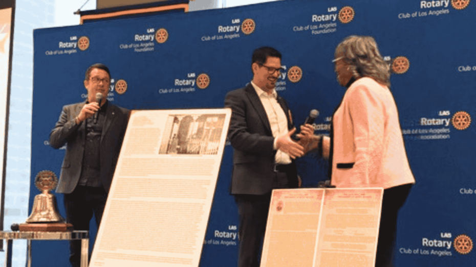 Jackie Broxton, wearing a pink blazer, shakes the hand of a man on stage